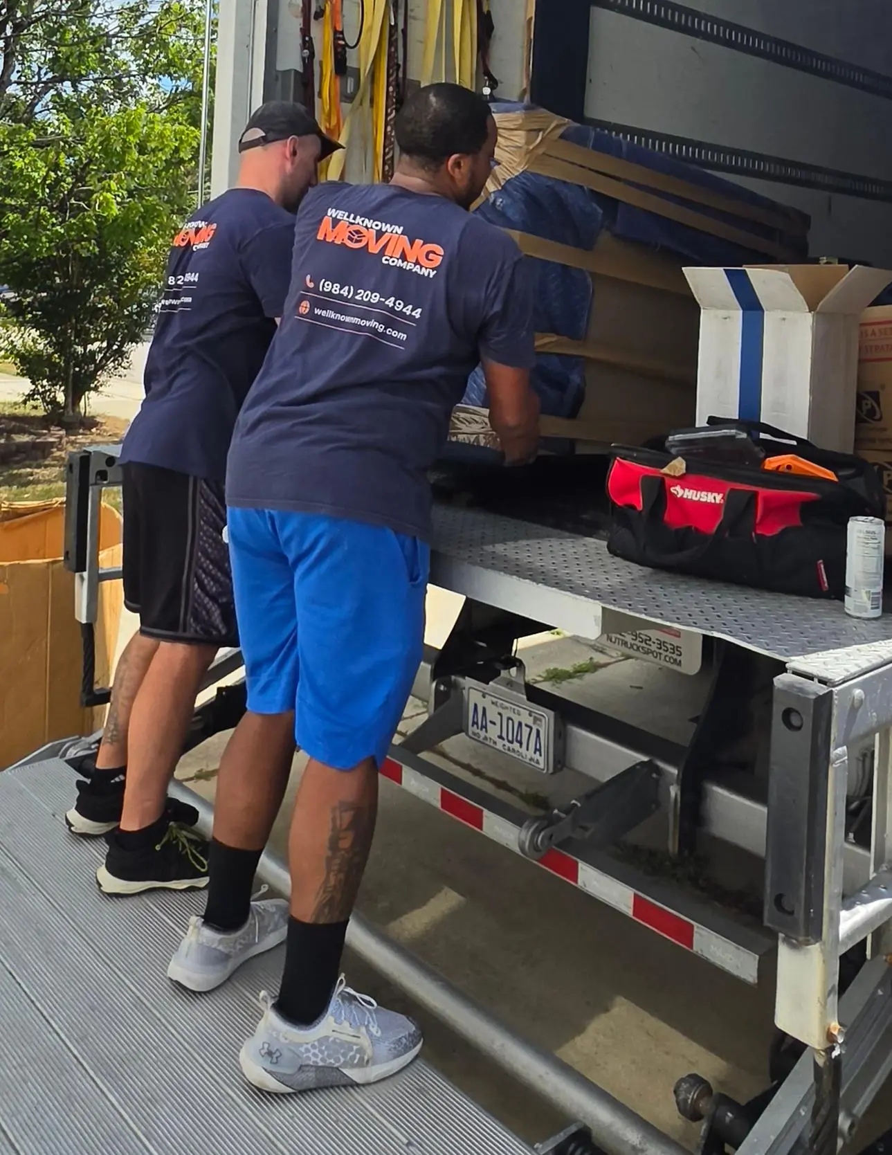 Two WellKnown movers loading padded furniture onto the truck liftgate